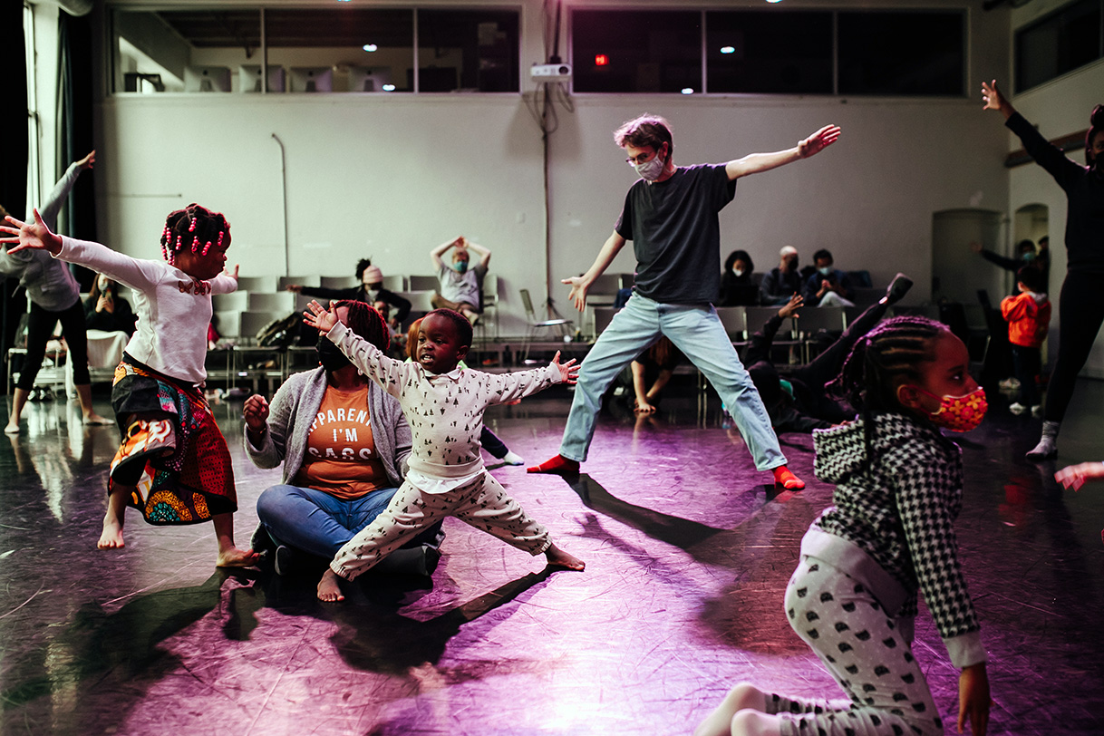 Image of a family dance class in a studio -- multiple people seen with outstretched arms
