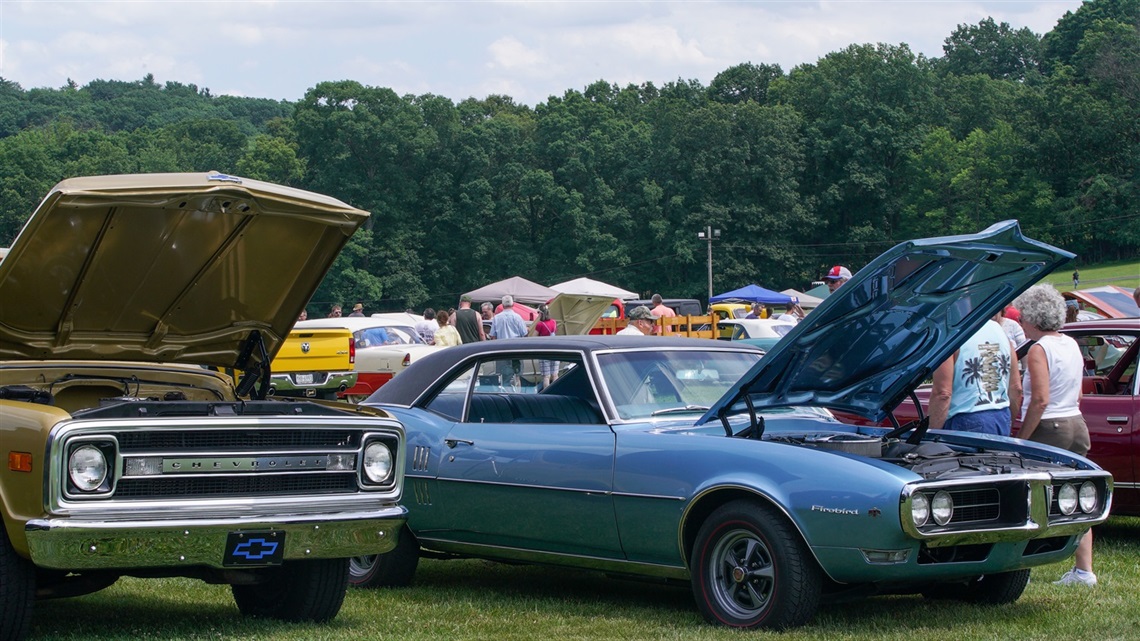 Photograph of people walking among classic cars in a park