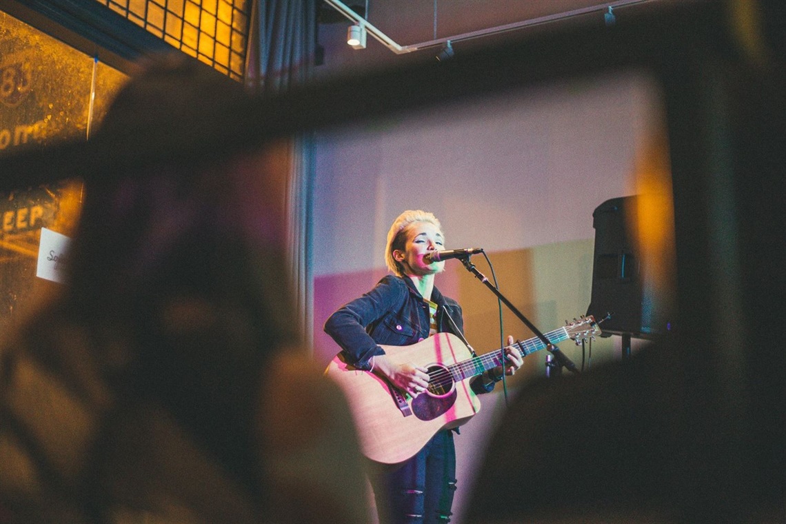 Photo of Noa Jordan singing on stage with a guitar