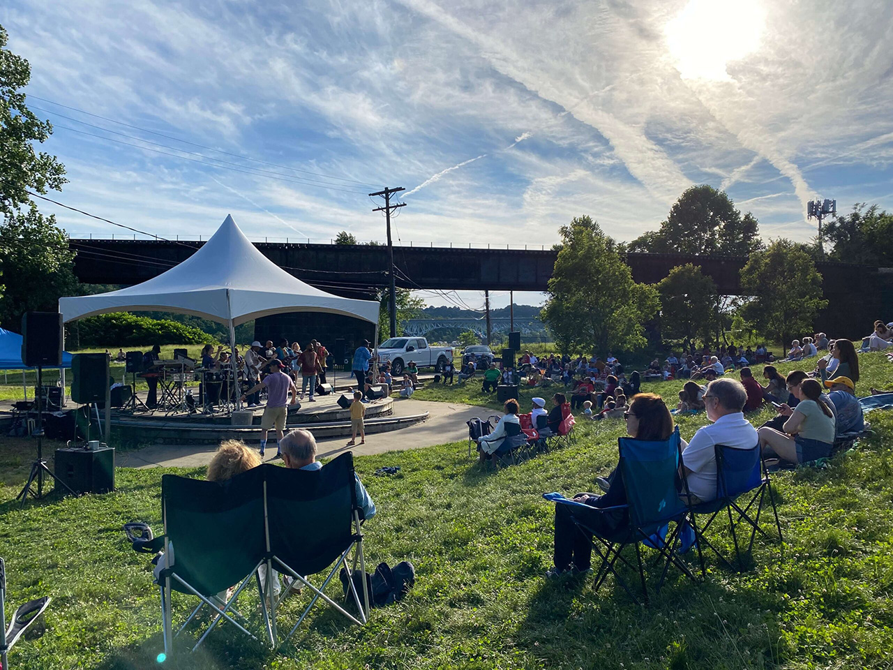 Sunset photograph of people sitting in lawn chairs watching a band on stage